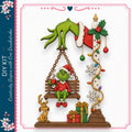 A whimsical Christmas scene featuring a Grinch sitting on a swing, with a reindeer, gift, and other holiday decorations surrounding him.