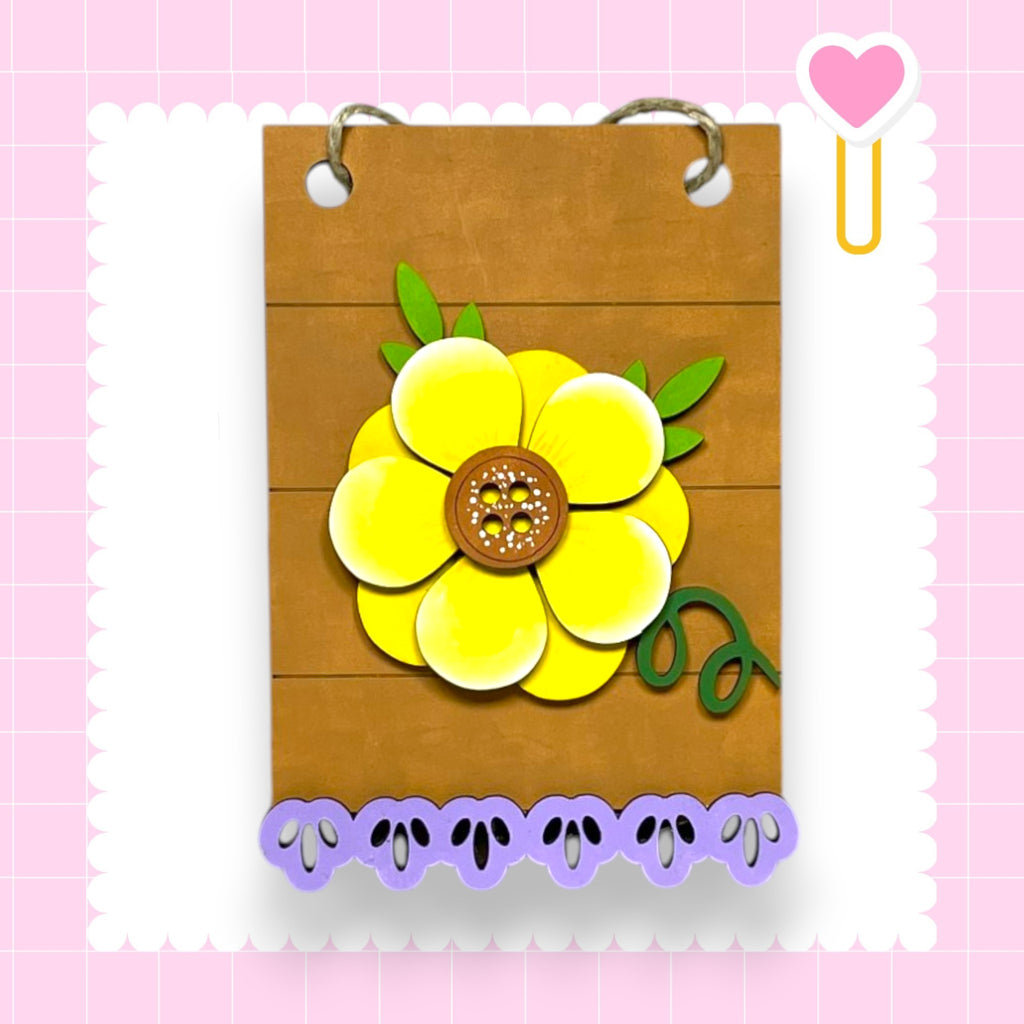 A wooden frame with a large yellow flower design on it, surrounded by purple cutout shapes.