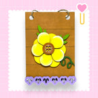 A wooden frame with a large yellow flower design on it, surrounded by purple cutout shapes.
