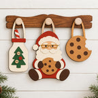 A wooden board with three wooden cutouts of Santa Claus, a Christmas tree, and a cookie, all hanging on a wooden hook.