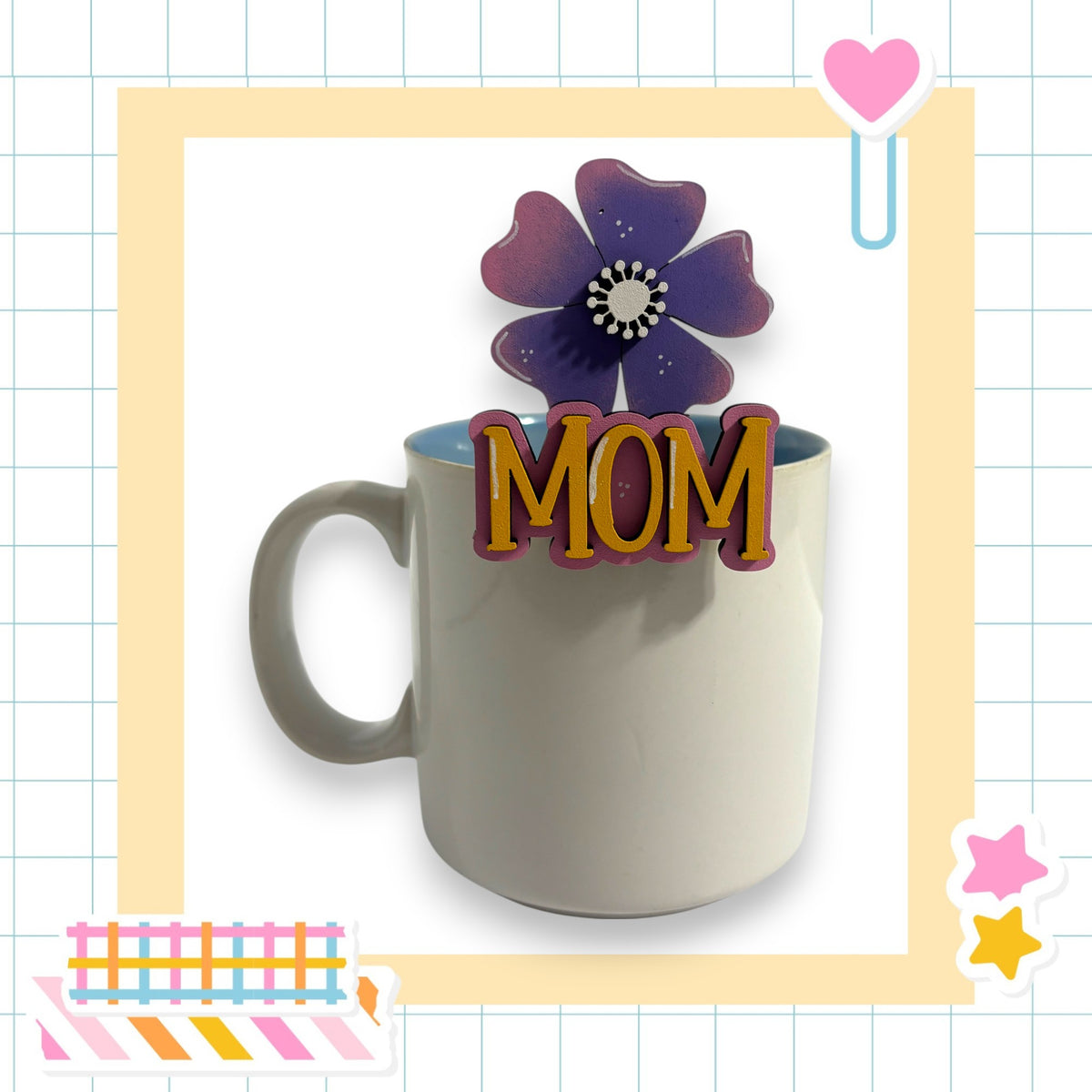 A white mug with the word "MOM" written on it, placed on a table surrounded by various colorful and decorative elements.