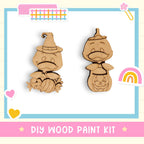 The image is a DIY wood paint kit featuring two wooden characters, a witch and a pumpkin, with a rainbow and hearts as decorative elements.