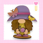 A whimsical wooden gnome figure wearing a purple hat with a pink ribbon and holding a snail, set against a pink background with a heart shape.