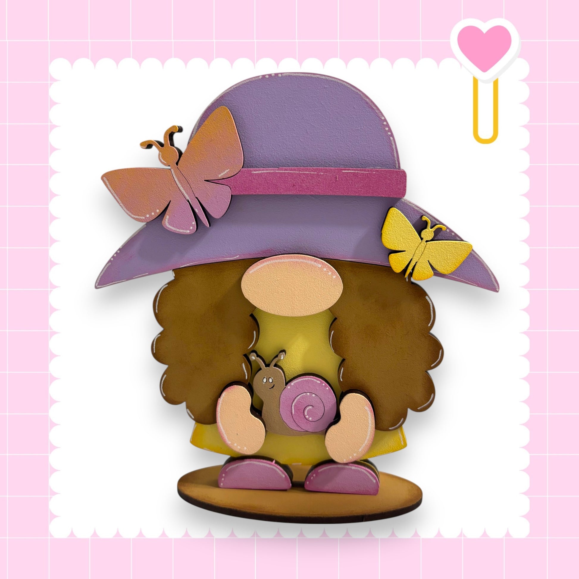 A whimsical wooden gnome figure wearing a purple hat with a pink ribbon and holding a snail, set against a pink background with a heart shape.