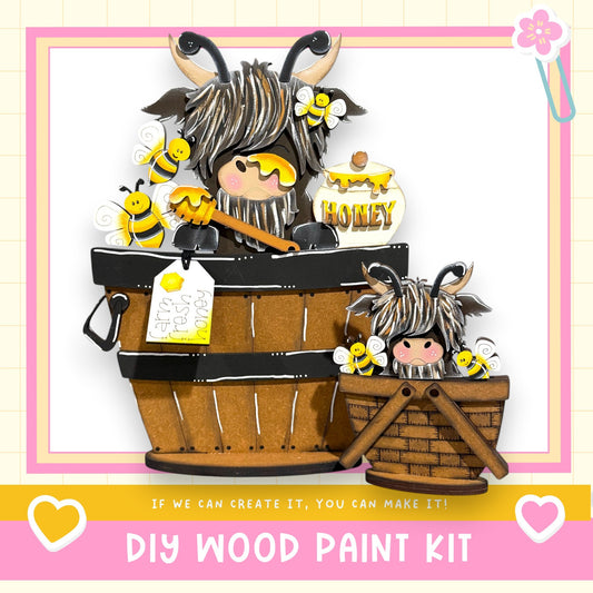 A wooden paint kit featuring a whimsical scene with a large wooden barrel and a smaller wooden basket filled with bees and honey. The kit is labeled "DIY WOOD PAINT KIT" and includes a heart symbol, suggesting it is a creative and fun project for people to make their own wooden paint.