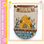 The image is a wooden sign featuring a beehive and the text "Busy bees make sweet days" in a decorative and playful style.