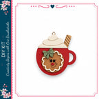 A wooden ornament in the shape of a mug with a gingerbread man design, featuring a red handle and a white whipped cream topping.