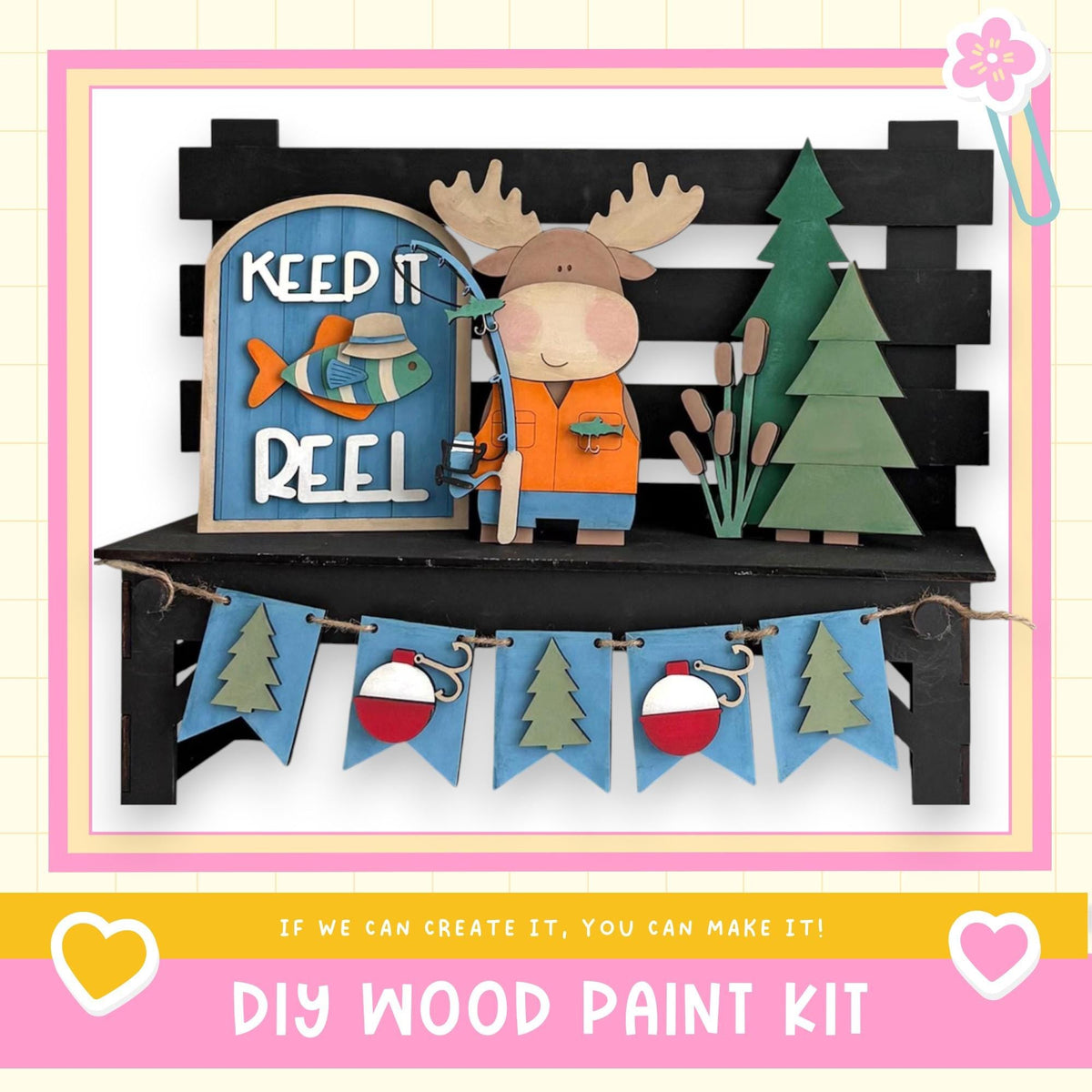 A DIY wood paint kit featuring a moose figure holding a fishing rod, surrounded by a "Keep it reel" sign, a bench, and a garland with Christmas trees.