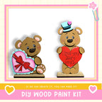 two wooden teddy bears, one holding a heart-shaped gift and the other holding a heart-shaped sign that says "I love you beary much". The bears are set against a pink and white background, and there is text at the bottom of the image that reads "DIY WOOD PAINT KIT" and "IF WE CAN CREATE IT, YOU CAN MAKE IT!".