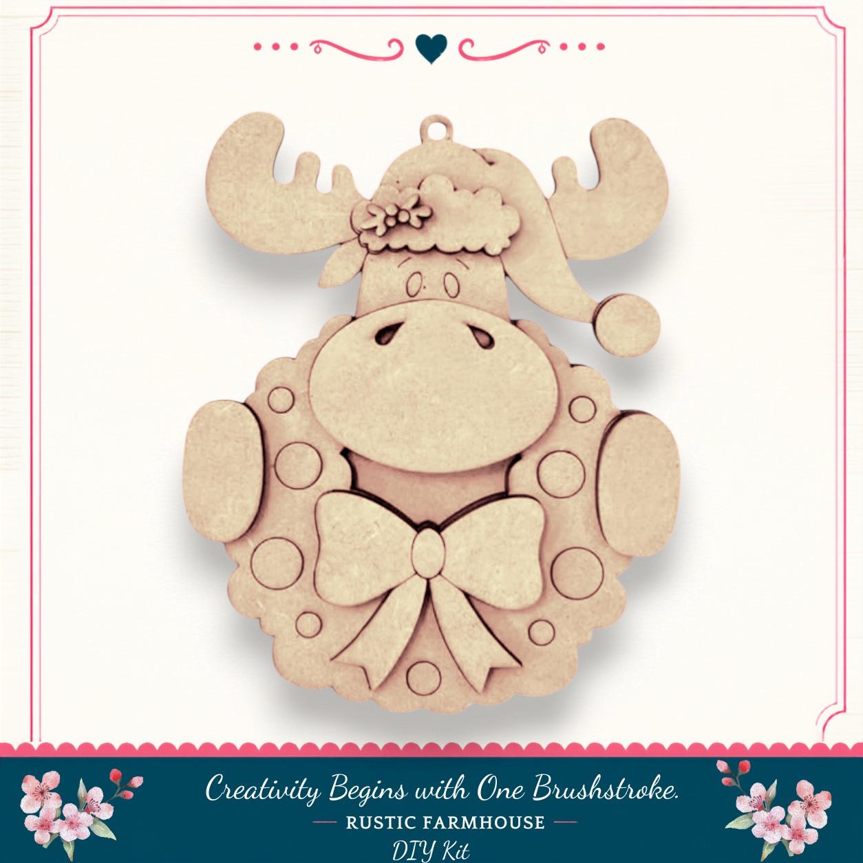 A wooden ornament in the shape of a moose wearing a wreath and a bow, with the caption "Creativity Begins with One Brushstroke. Rustic Farmhouse DIY Kit"