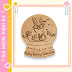 A wooden snow globe with a bunny inside, surrounded by flowers, and the text "Every Bunny Welcome" written on it.