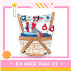 The image is a colorful and playful DIY wood paint kit, featuring a basket filled with various paint-related items such as a paintbrush, a paint roller, and a paint palette. The kit appears to be designed for children, with a cheerful and creative theme.