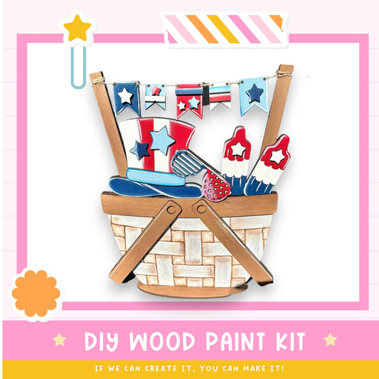 The image is a colorful and playful DIY wood paint kit, featuring a basket filled with various paint-related items such as a paintbrush, a paint roller, and a paint palette. The kit appears to be designed for children, with a cheerful and creative theme.