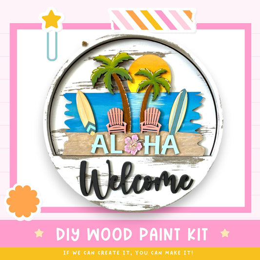 The image is a colorful and vibrant DIY wood paint kit for creating a "Aloha Welcome" sign. It features a circular design with a beach scene, palm trees, surfboards, and a "Aloha" greeting. The kit includes the necessary materials and instructions for creating the sign, encouraging viewers to "If we can create it, you can make it!"