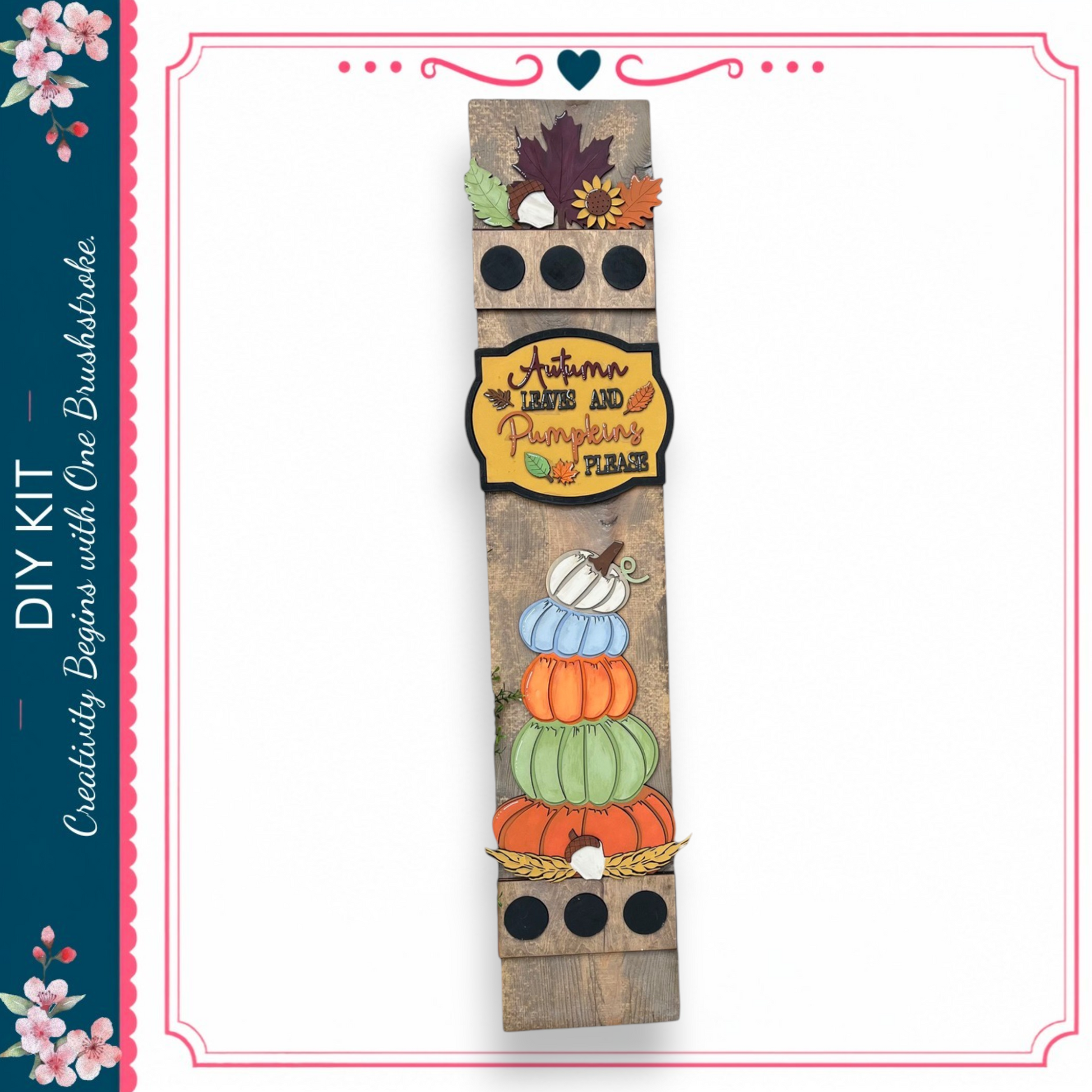 a wooden sign with a decorative design, including a stack of pumpkins and autumn leaves. The sign is surrounded by a border and has a heart-shaped decoration at the top.