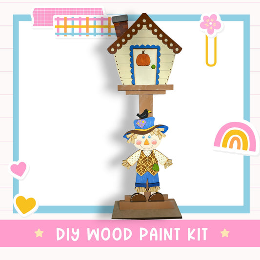 a DIY wood paint kit, including a wooden birdhouse and a scarecrow figure, with a colorful and whimsical design.