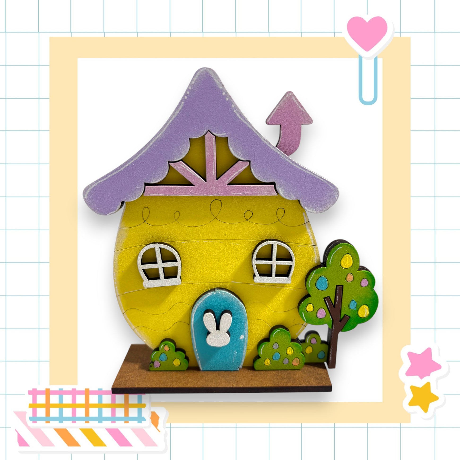A colorful, whimsical toy house with a purple roof, white windows, and a blue door, set against a grid background with a heart and stars.