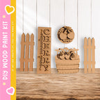a collection of wooden cutouts, including a large wooden sign with the word "CHERRY" carved into it, a wooden fence, and a wooden basket filled with fruit. The objects are arranged on a wooden surface, creating a rustic and charming scene.