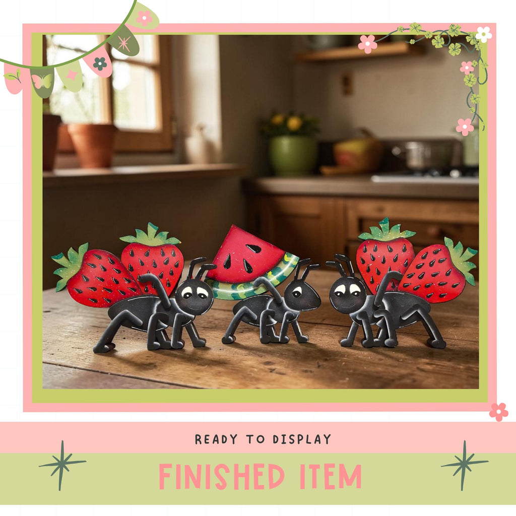 a group of four toy insects, including two ants and two ladybugs, each carrying a strawberry. The insects are arranged on a wooden surface, with a window and a potted plant visible in the background. The image is framed with a pink border and the text "READY TO DISPLAY FINISHED ITEM" is displayed at the bottom.
