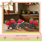 a group of four toy insects, including two ants and two ladybugs, each carrying a strawberry. The insects are arranged on a wooden surface, with a window and a potted plant visible in the background. The image is framed with a pink border and the text "READY TO DISPLAY FINISHED ITEM" is displayed at the bottom.