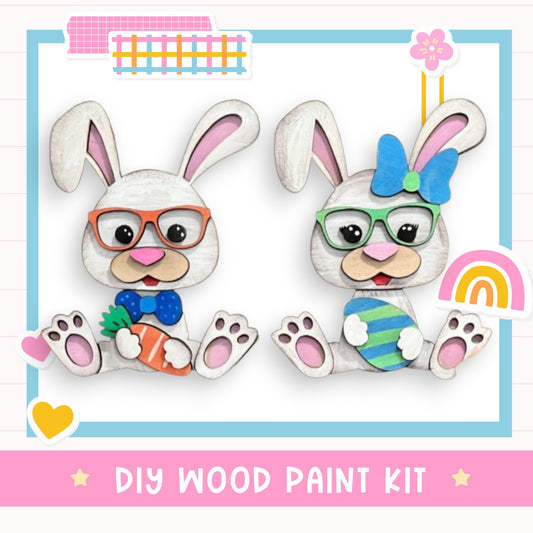 two cute wooden rabbits wearing glasses and holding Easter eggs, with a DIY wood paint kit labeled "DIY WOOD PAINT KIT" in the background.