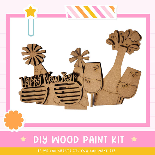 The image is a DIY wood paint kit featuring a variety of wooden shapes and objects, including a star, a windmill, and a pair of sunglasses, all set against a pink and white background.