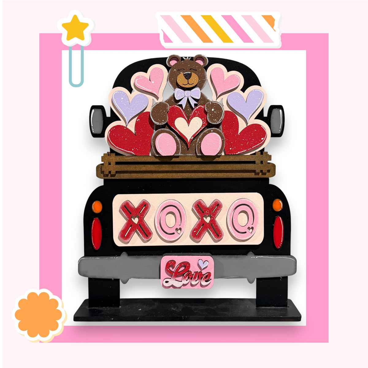A wooden truck with a teddy bear sitting on top of it, surrounded by heart-shaped cutouts.