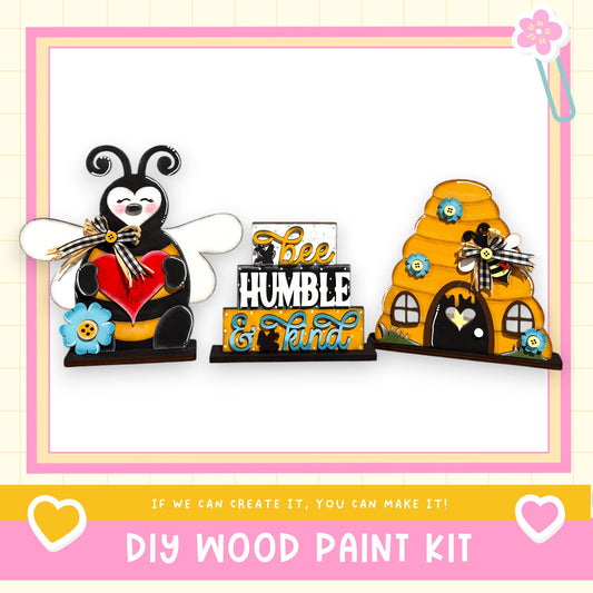 a DIY wood paint kit with a bee and a beehive as the main decorative elements. The kit includes a wooden frame with a bee and a beehive, as well as a sign that says "bee humble & art". The kit is designed to encourage creativity and craftsmanship, as it states "If we can create it, you can make it!"