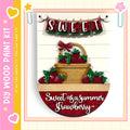 The image is a decorative piece featuring a basket filled with red strawberries, with the word "Sweet" written above it. The basket is placed on a wooden surface, and the background is white with a pink border.