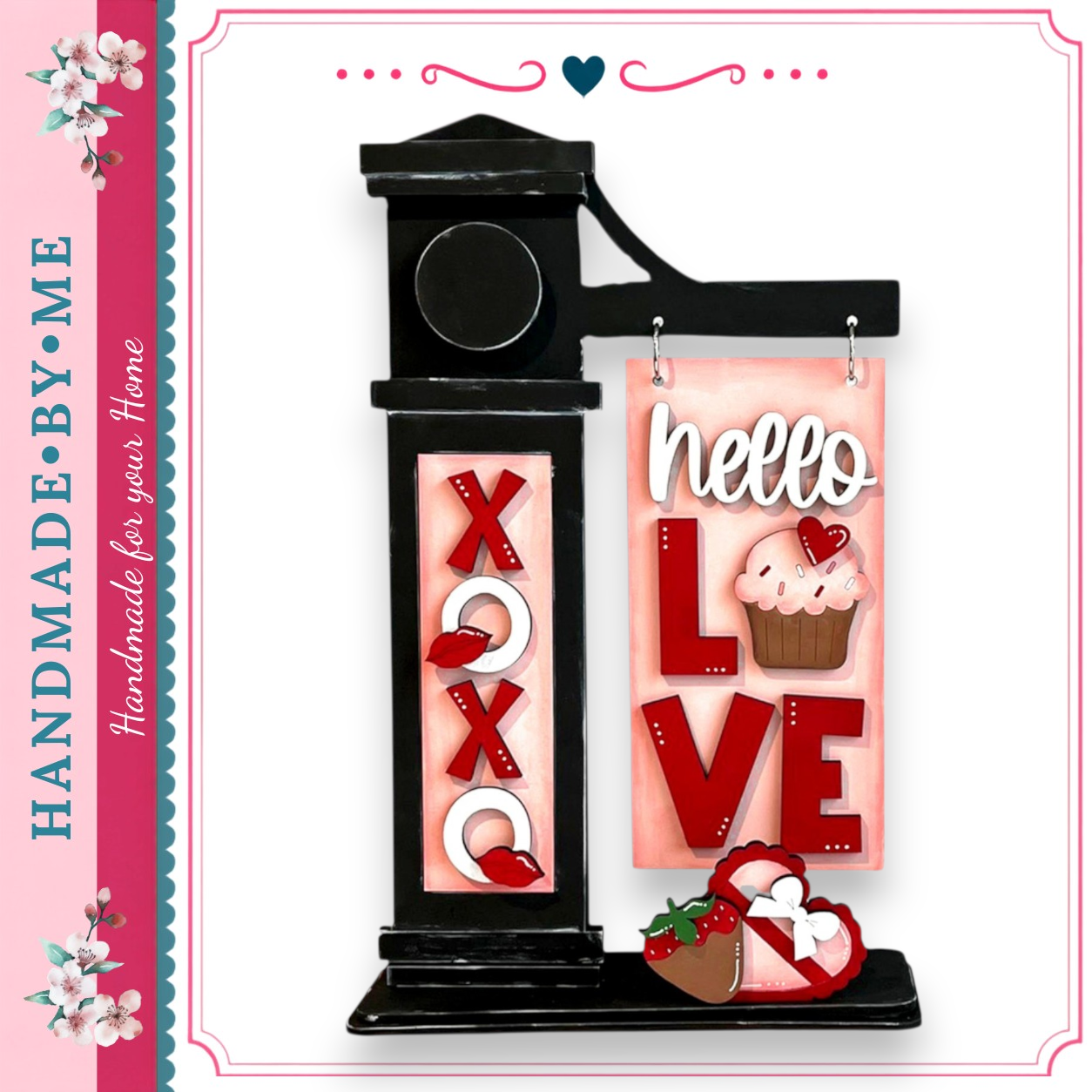 A handmade sign with the words "Hello Love" displayed on it, along with a cupcake and a heart. The sign is black and features decorative elements such as the word "XO" and the word "LOVE".