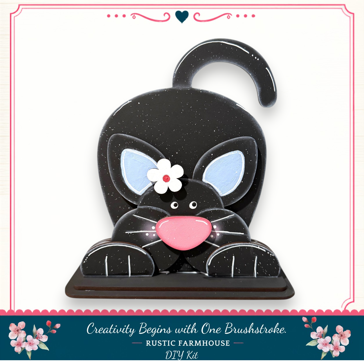 A black cat-shaped object with a pink nose and a white flower on its face, sitting on a wooden base.