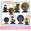 The image is a collage of various decorative items, including snow globes, wooden signs, and camping-themed objects, all set against a white background.