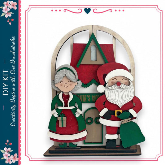 A wooden Christmas-themed display featuring a Santa Claus figure and an elderly woman, likely representing the "Santa's Workshop" as indicated by the text on the display.