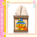 A wooden tissue box with a cartoon duck wearing a witch's hat and holding a pumpkin, set against a pink and yellow background with decorative elements.