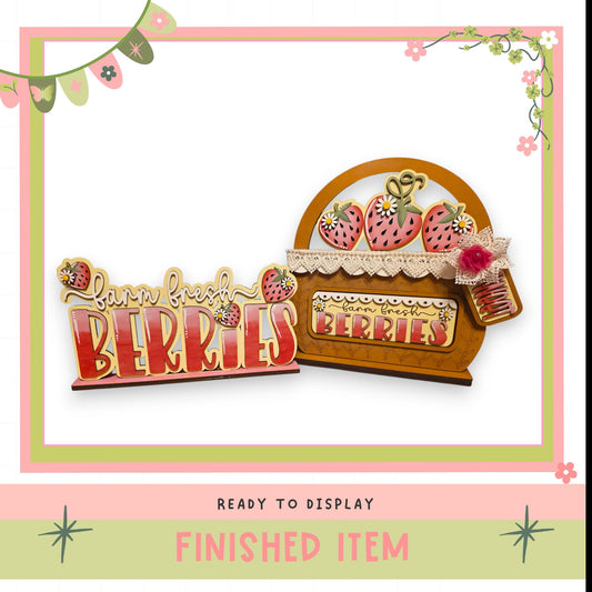 a wooden sign with the word "BERRIES" written on it, along with a basket of strawberries. The sign and basket are displayed in a pink and green frame, and the image is described as a finished item, ready to be displayed.
