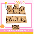 The image is a promotional poster for a DIY wood paint kit, featuring three wooden snowmen and the word "WINTER" written on a wooden block.