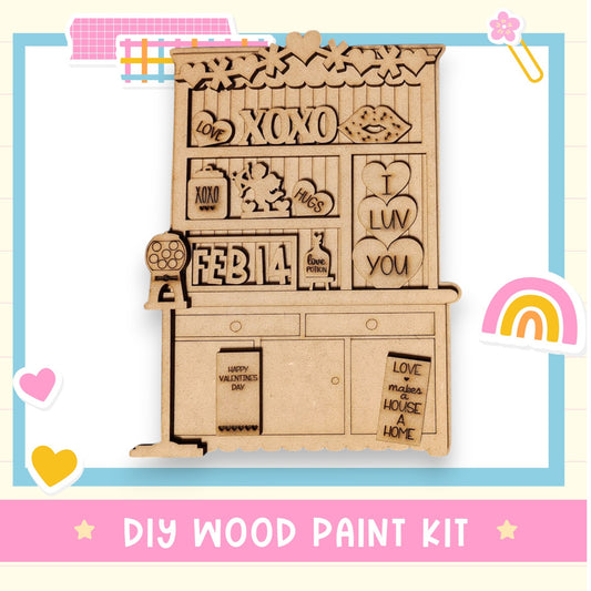 The image is a wooden paint kit with various decorative elements, including a wooden shelf with a "XOXO" sign, a "I LOV YOU" sign, and a "HAPPY VALENTINE'S DAY" sign. The kit appears to be a DIY project for creating a wooden frame or decoration.