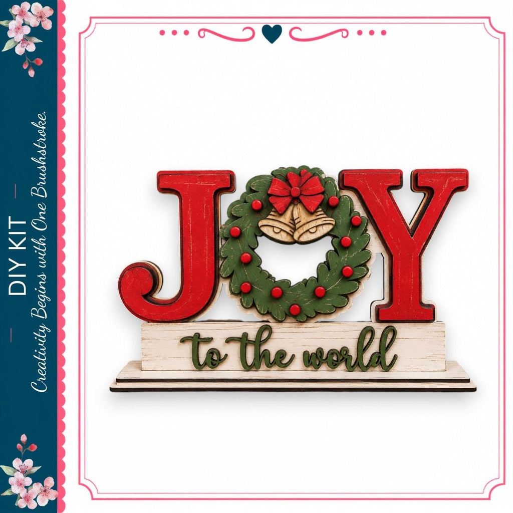 a wooden sign with the word "Joy" written on it, along with a wreath and bells. The sign is displayed against a white background, and there is a decorative border around the edges.