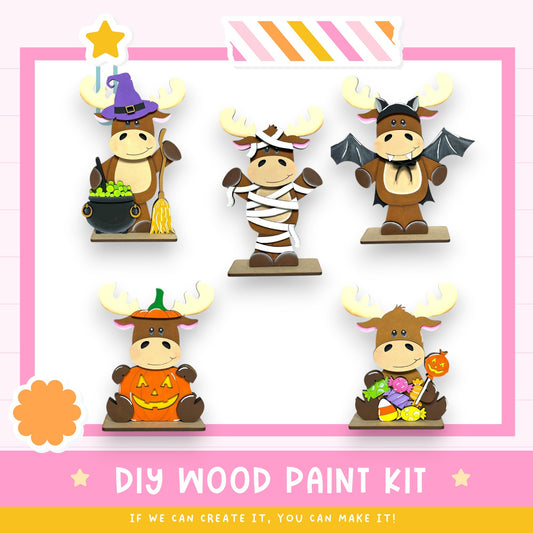 a DIY wood paint kit with five moose figurines dressed in various costumes, including a witch hat, a mummy, a bat, a pumpkin, and a candy cane.