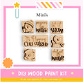 The image is a promotional poster for a DIY wood paint kit, featuring six wooden snowman stickers with winter-themed phrases.