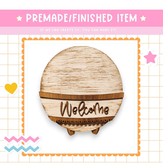 a wooden welcome sign with the word "Welcome" written on it, surrounded by decorative elements such as a heart, a star, and a zigzag pattern.