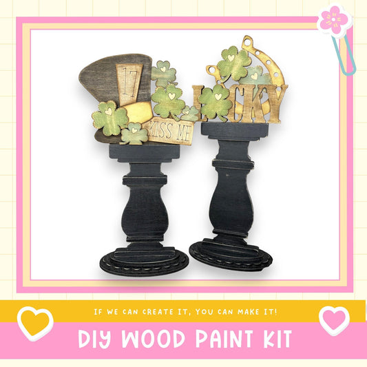 a DIY wood paint kit, with two black wooden stands holding various decorative items such as a hat, a sign, and a cloverleaf pattern. The text "If we can create it, you can make it!" is displayed, suggesting that the kit is designed for individuals to create their own unique and personalized wooden decorations.
