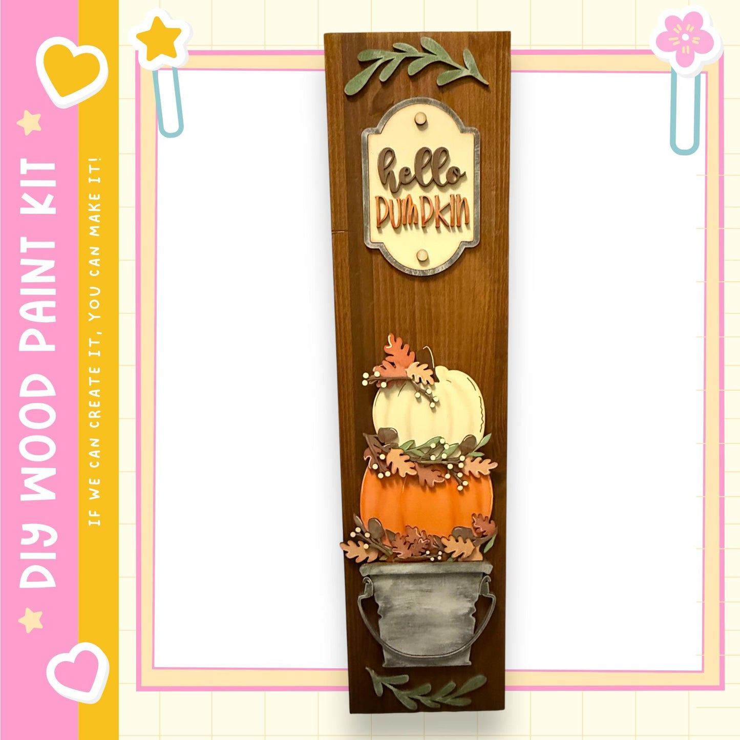a wooden display with a pumpkin and leaves, along with a sign that says "Hello Pumpkin". The display is set against a pink and yellow background with a heart and star motif.