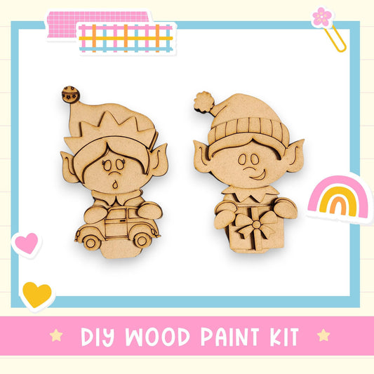 two wooden elf figurines, one standing and one sitting, along with a DIY wood paint kit and various decorative elements such as hearts and a rainbow.