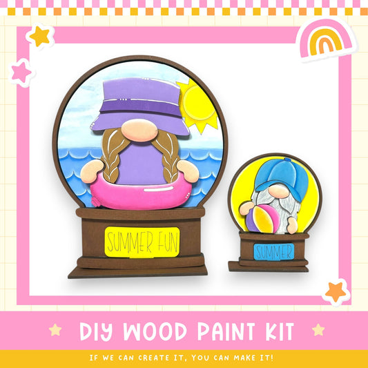 a DIY wood paint kit for creating a wooden snow globe, with two snow globes depicting gnomes. The kit includes a wooden base and a label that reads "SUMMER FUN". The kit is designed for people to create their own wooden snow globes, allowing them to customize the design and create a unique winter-themed decoration.