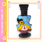 a wooden paint kit with a whimsical design, including a blue hat with a bird perched on it and a flower.