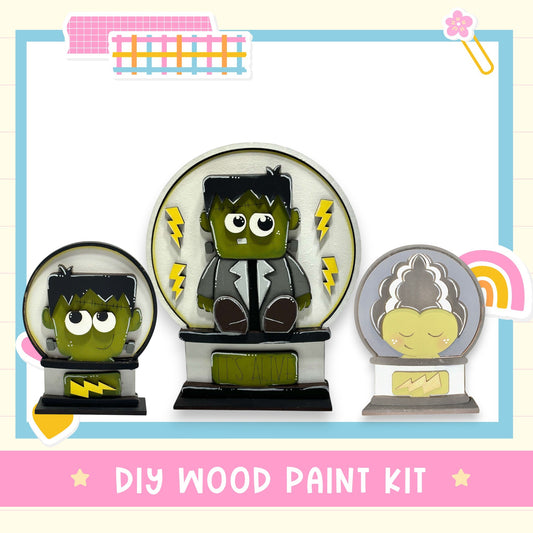 a DIY wood paint kit with three cartoon-style figures, including a green monster, a person, and a woman, all sitting on a circular base.