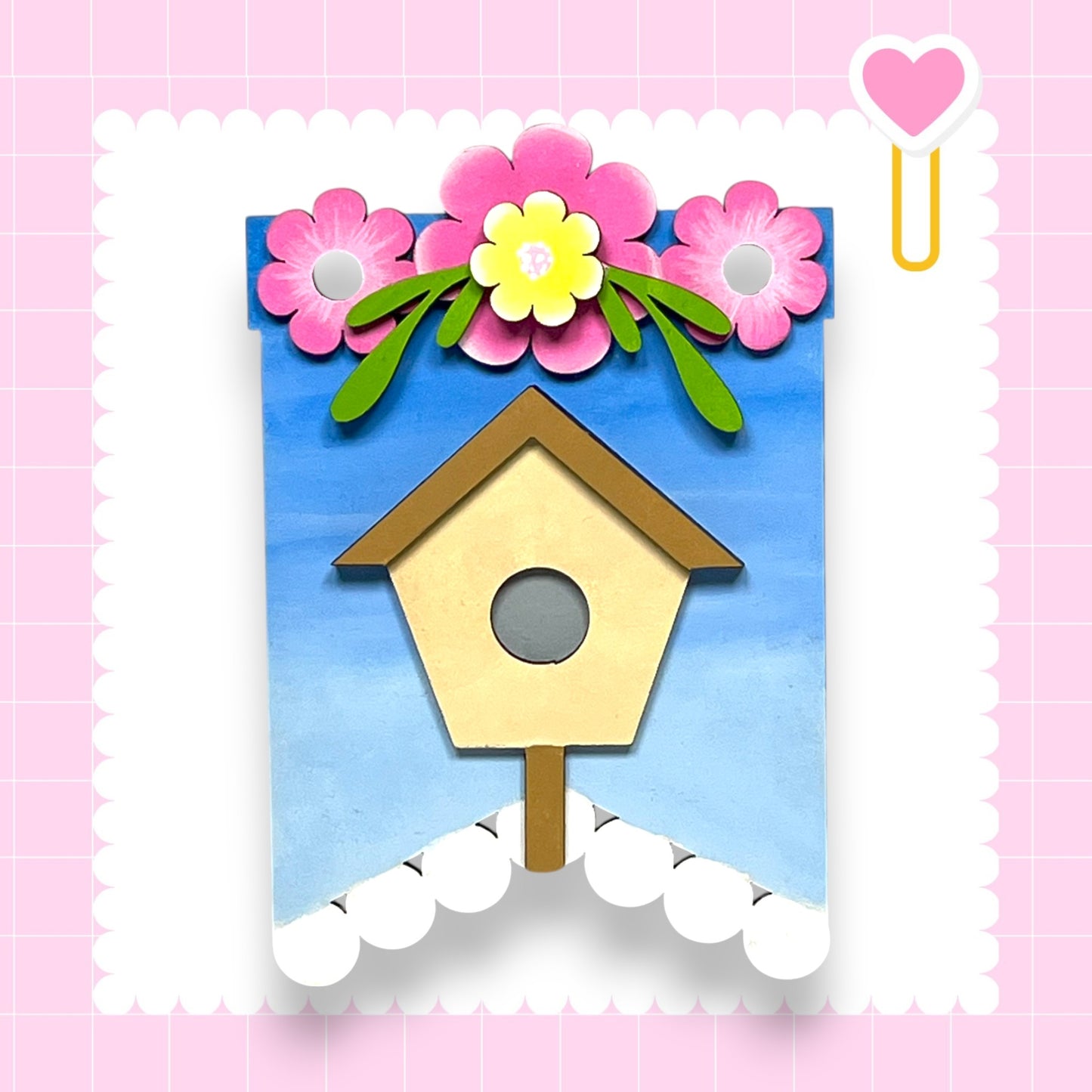 A colorful birdhouse with flowers on top, set against a pink and white background.