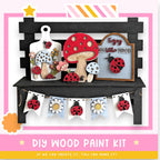 The image is a DIY wood paint kit featuring a variety of wooden cutouts, including mushrooms, ladybugs, and flowers, arranged on a black shelf. The kit appears to be made of wood and is designed for painting.