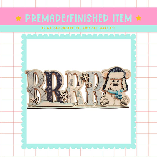 a wooden sign with the word "BRRR" made up of wooden letters, with a teddy bear sitting on top of the letters.